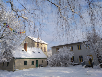 Blick unter den kahlen Birkenzweigen durch auf den eingeschneiten Hof und die drei Häuser.